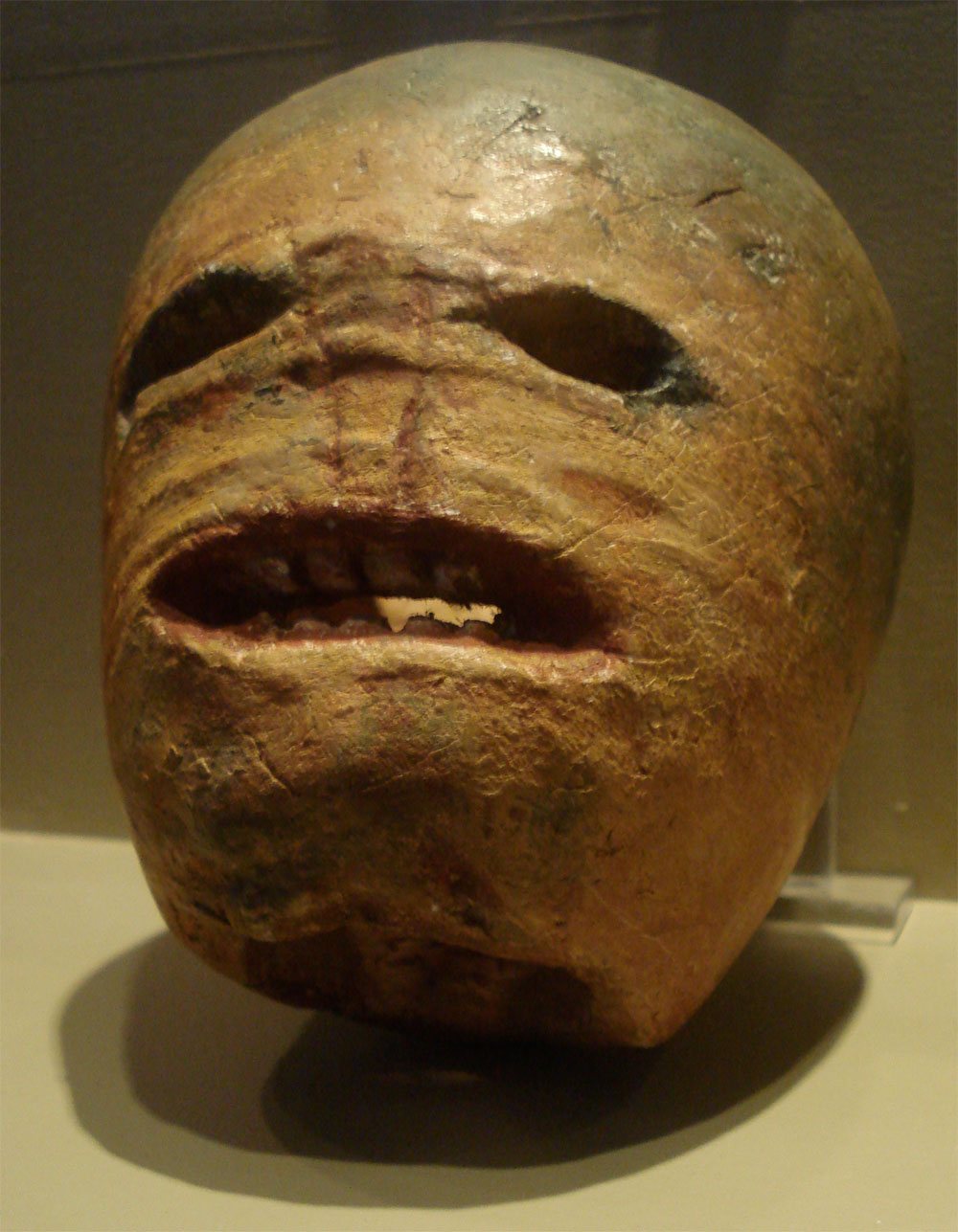 A traditional Irish jack-o'-lantern carved from a turnip, with two hollow eyes and a wide open mouth full of uneven teeth, displayed in a museum case